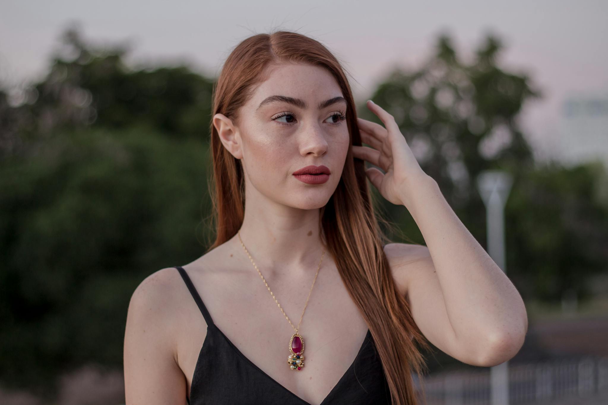 Stunning portrait of a woman wearing a gold necklace, set outdoors with a natural background.